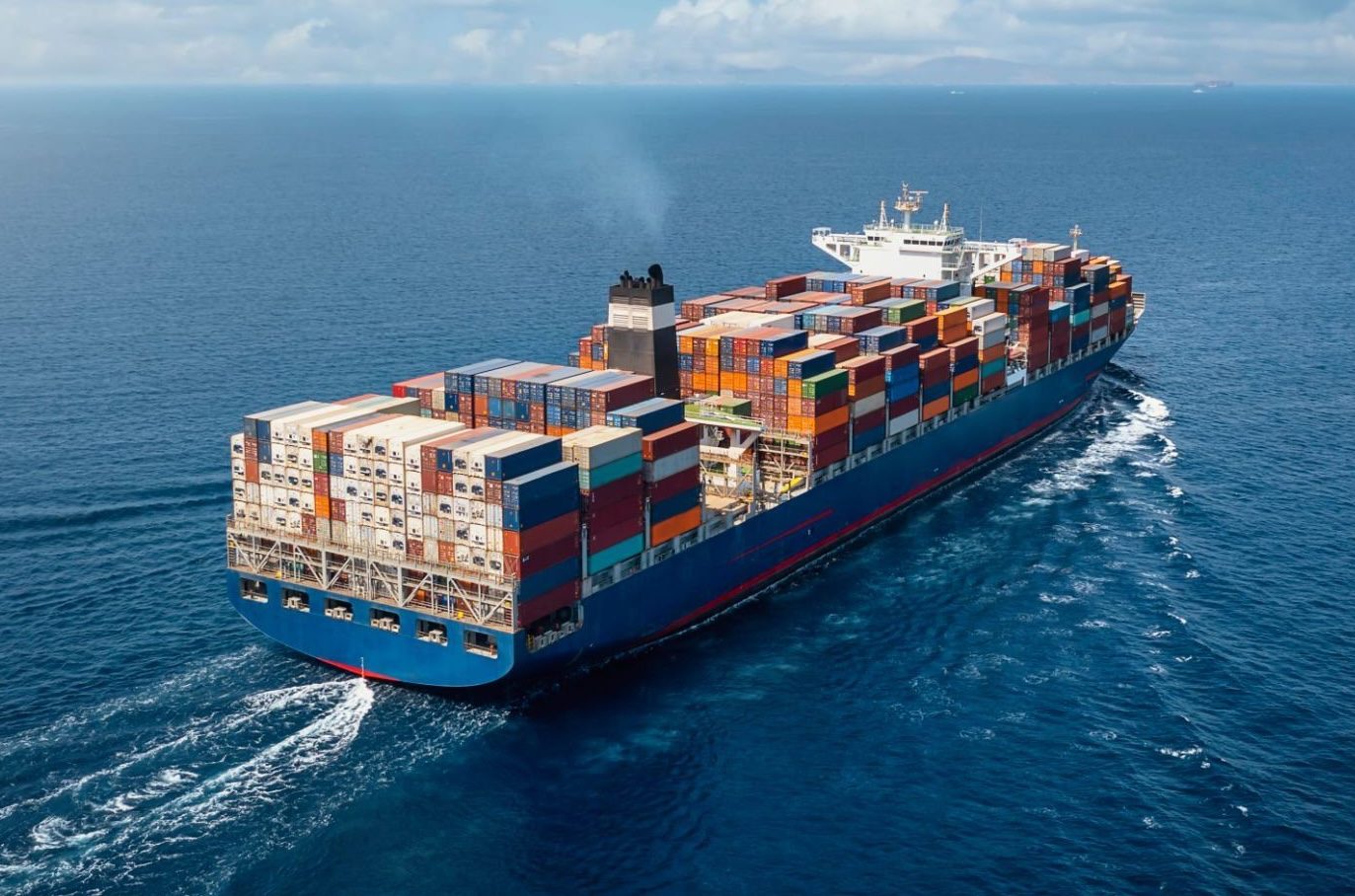 A large container cargo ship travels over calm, blue ocean